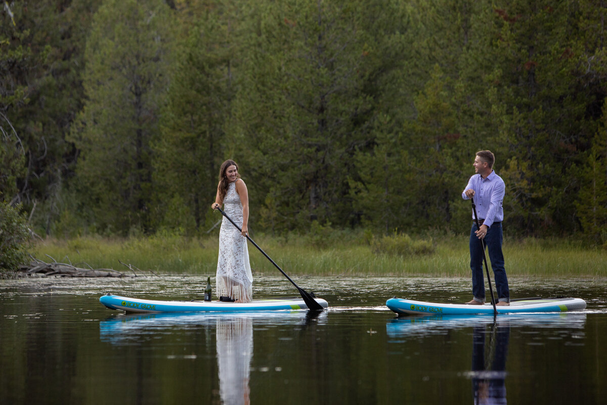 A bride and groom paddle boarding on a lake in Idaho.