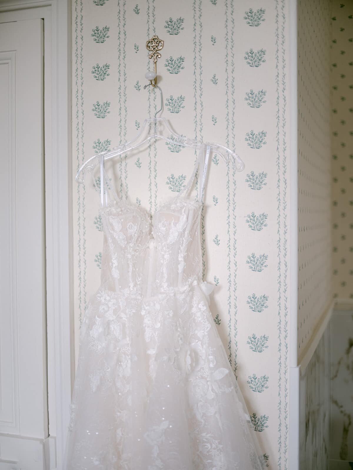 Elegant lace wedding dress hanging in a classic French room, photographed by Paris wedding photographer Thomas Raboteur