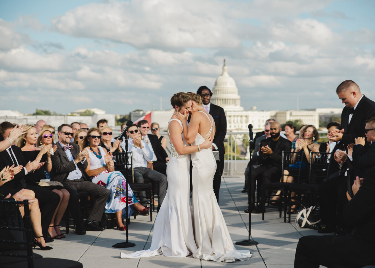 Two brides hugging with wedding guests sitting on either side of them