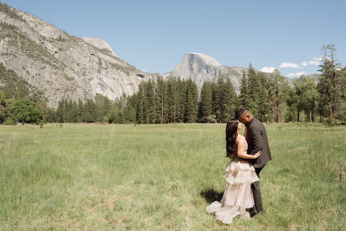 Engaged couple in fields in Yosemite California holding each other with the silhouette of the mountains in the background