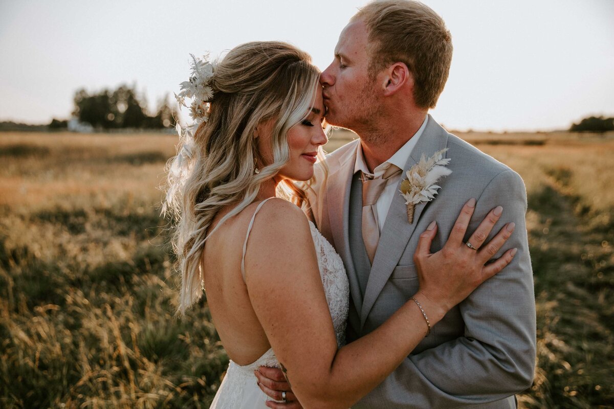 Formal wedding photo of bride and groom at rustic barn wedding in Exeter, ON. Bride and groom are embracing each other. The bride has her eyes closed with her arm on the grooms chest. The groom is kissing her forehead.