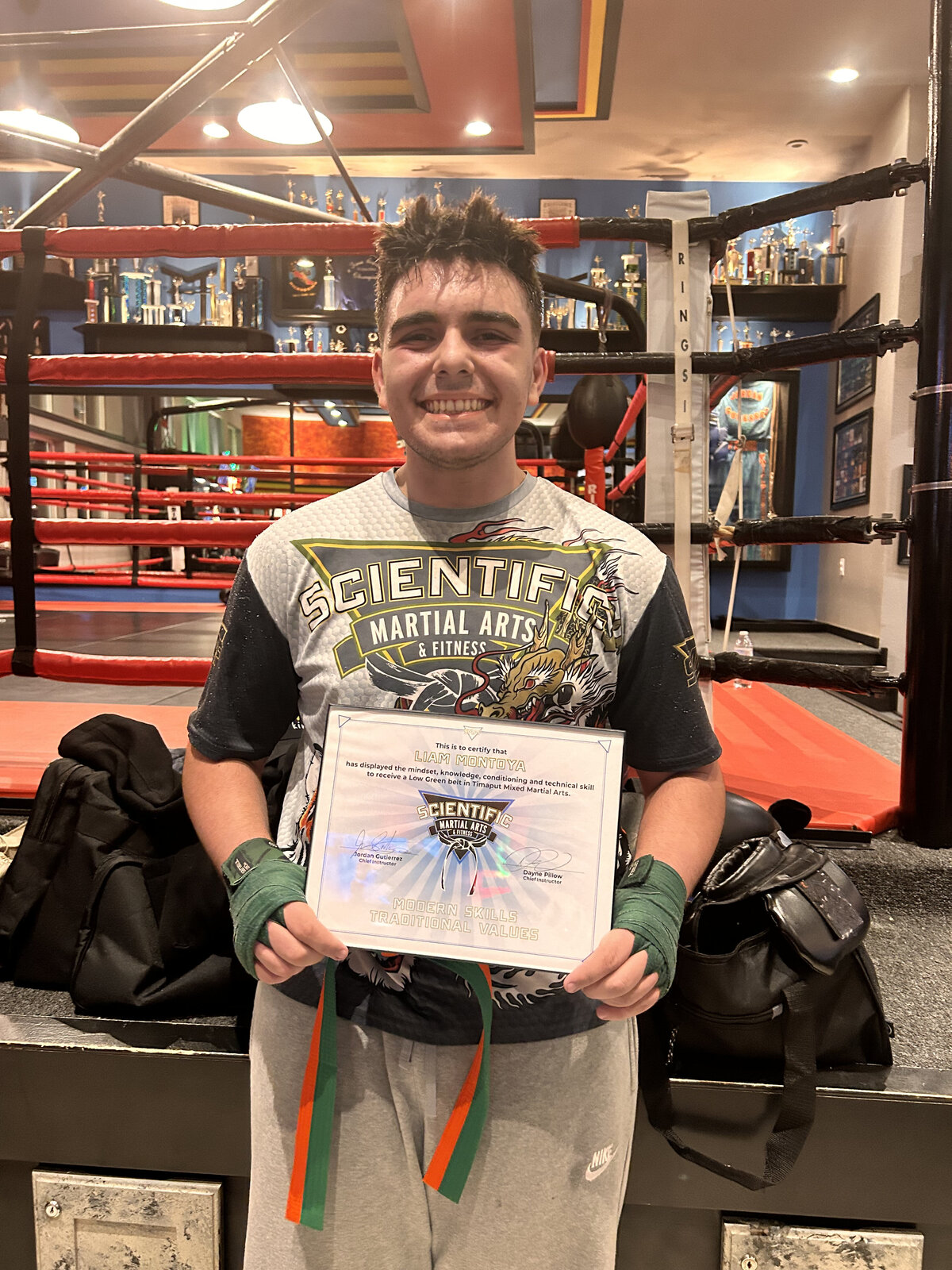 teenage boy holds a certificate while passing an MMA class