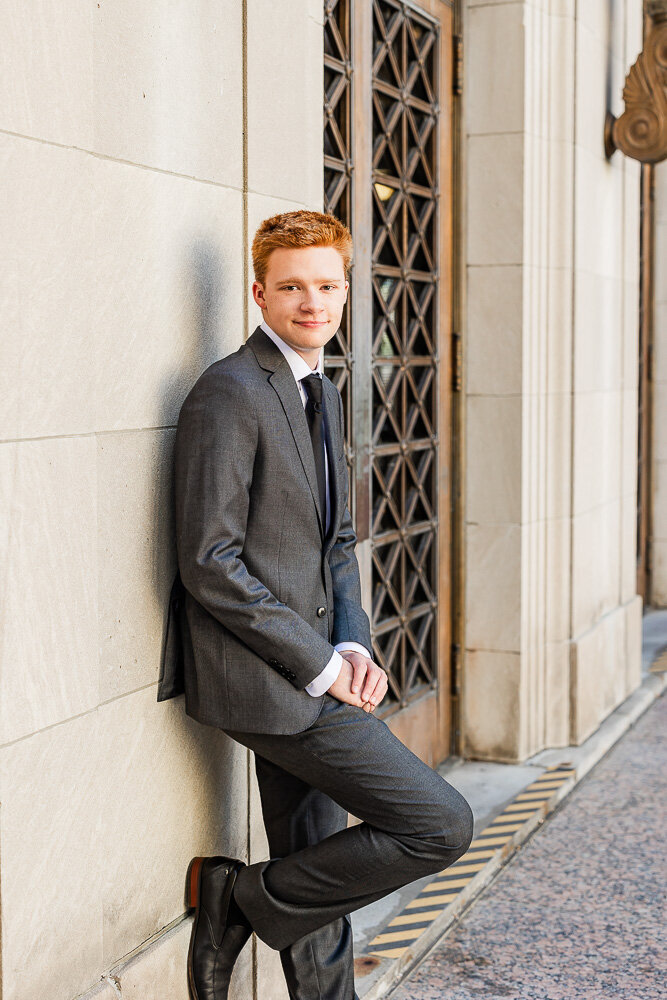 Boy in a suit casually leaning against an old building