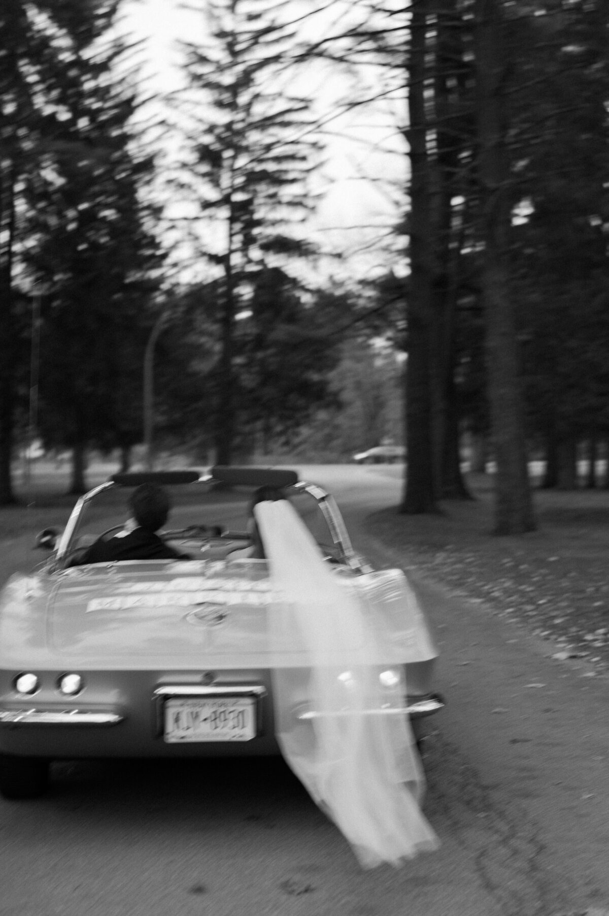 Bride and groom drive away in their convertible 