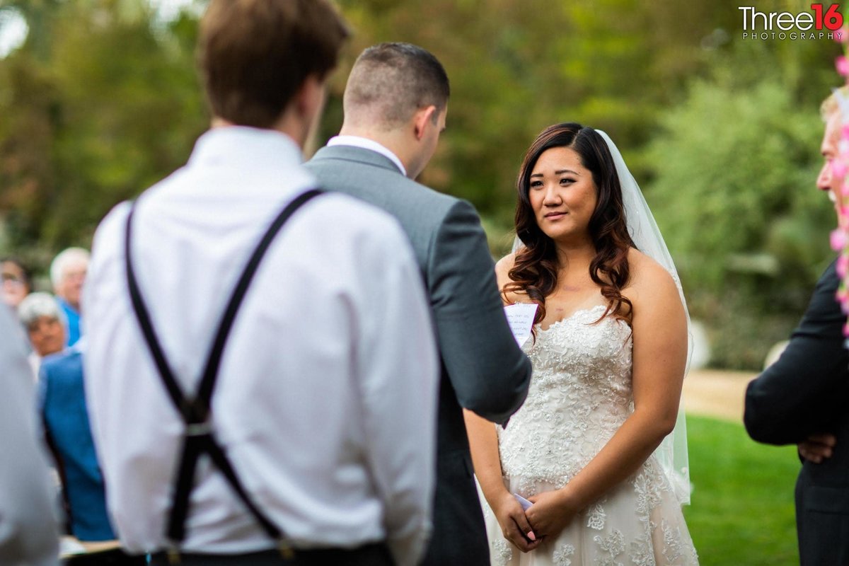 Bride looks at her Groom as he reads his wedding vows to her