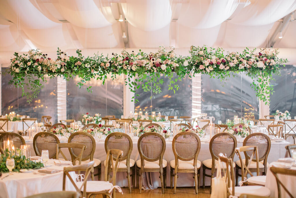 a hanging flower installation above the head table at pinecroft estate in cincinnati ohio with floral centerpieces along the table with velvet linen and candles