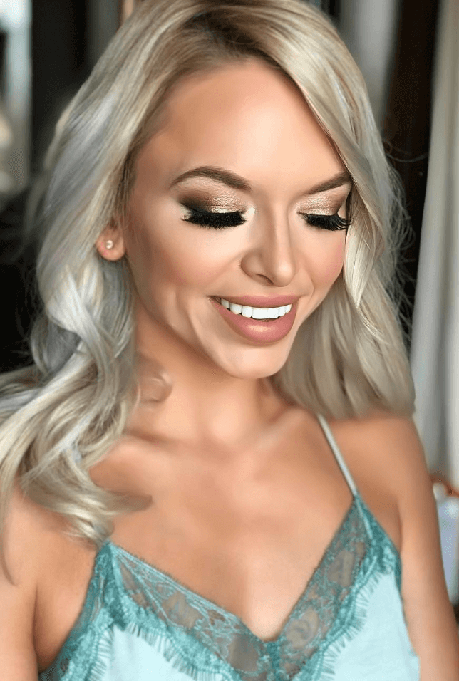 Smiling woman with voluminous lashes, golden eyeshadow, and soft curls wearing glam makeup by Mistique Makeup in San Antonio