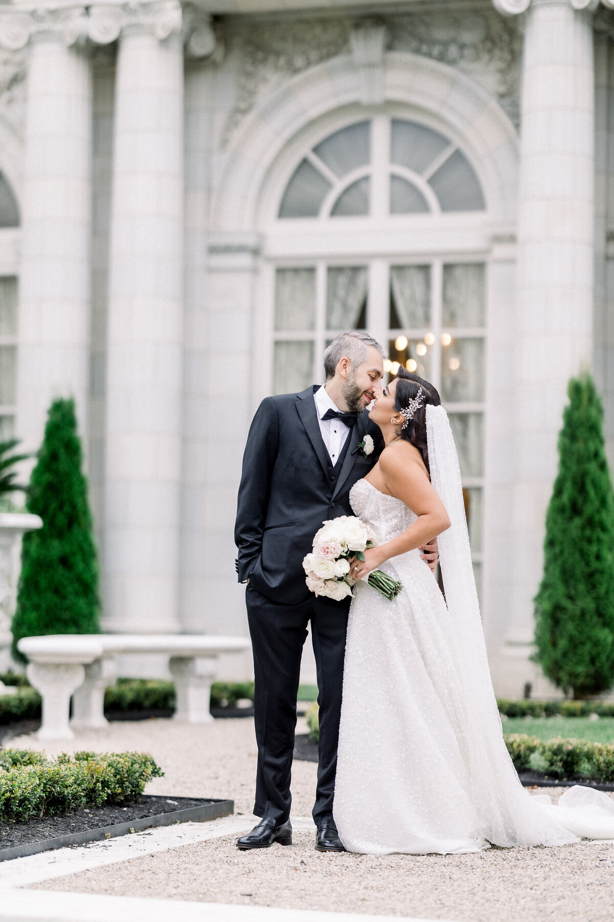sophisticated bride and groom  kiss outside during wedding day portraits outside of rosecliff mansion in newport rhode island, groom kisses her on the temple during first look