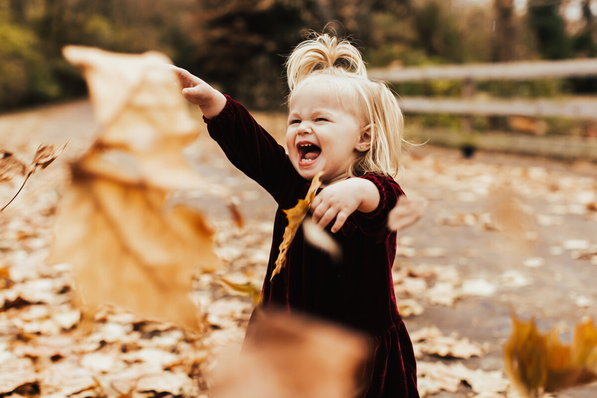 little girl laughing playing in fall leaves