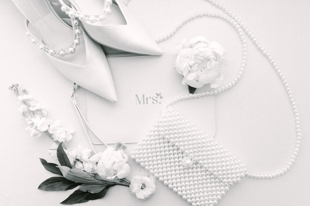 Flat lay of bridal accessories with shoes, pearls, and flowers