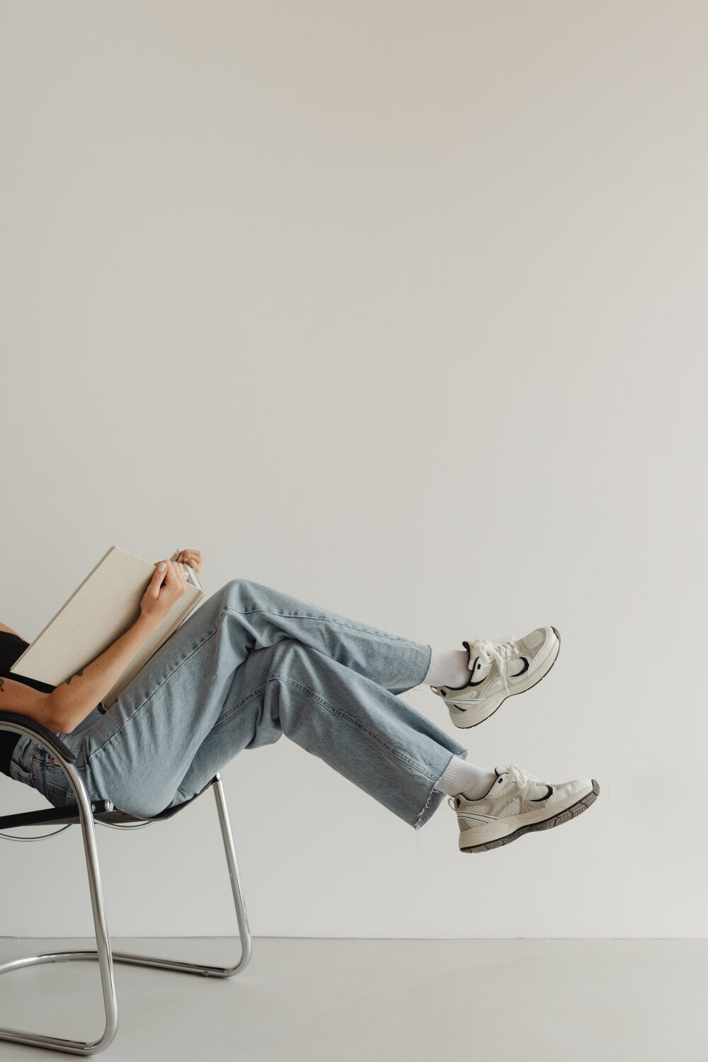 stock image of a woman in jeans sitting on a chair while holding a book