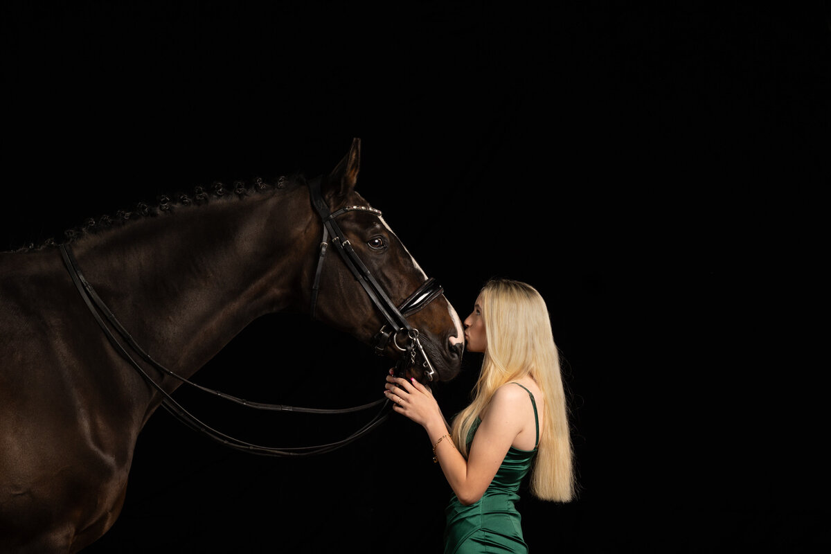 A studio portrait photo of a horse and a girl giving the horse a kiss on the nose