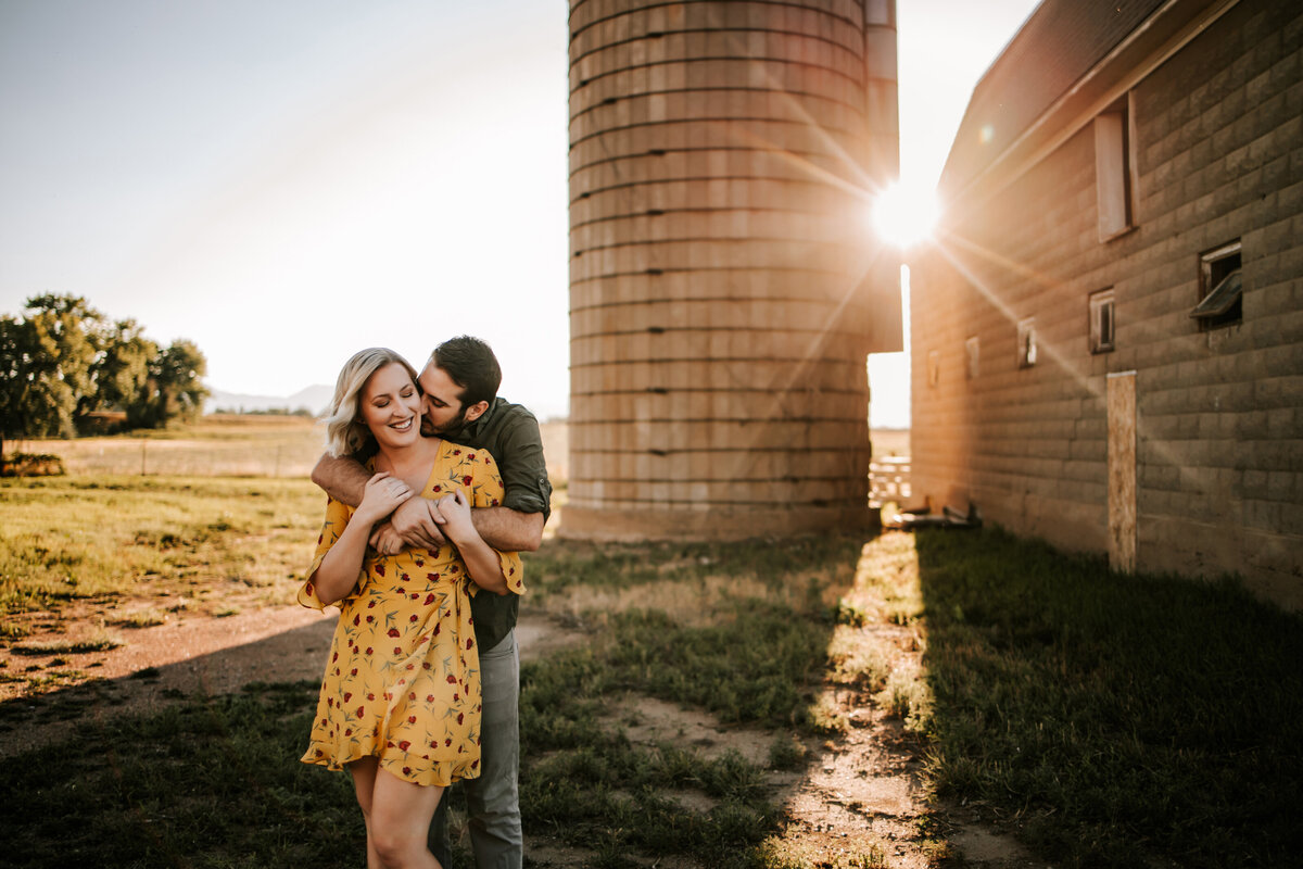 coloraddo couple hold eachother on famr land with a sun burst behind them for a couples session