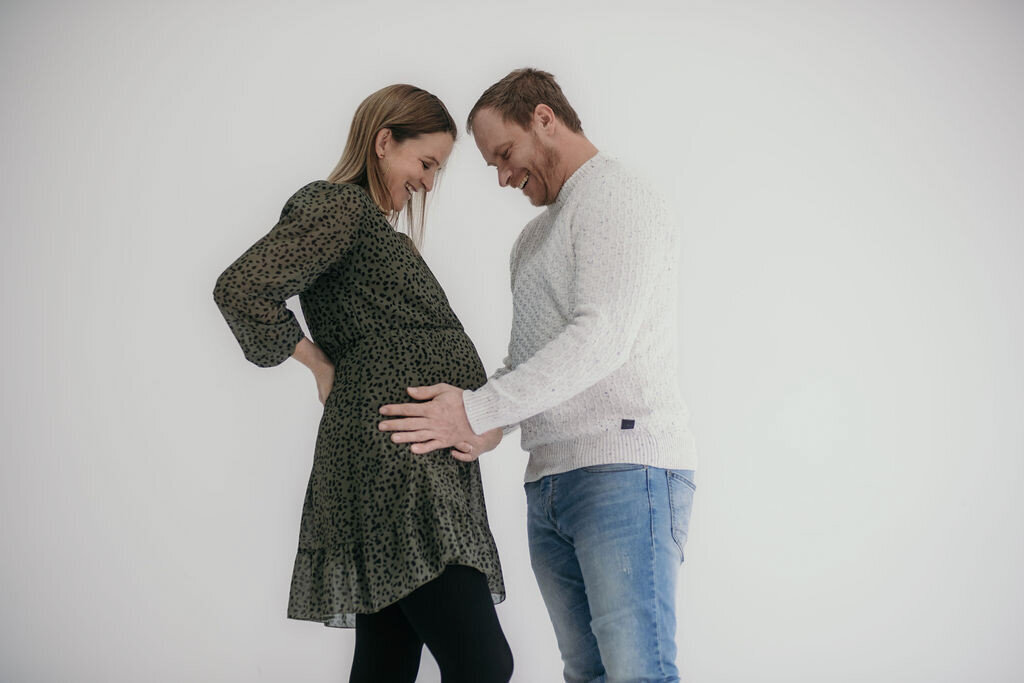 Expecting father holds the baby bump smiling happily.