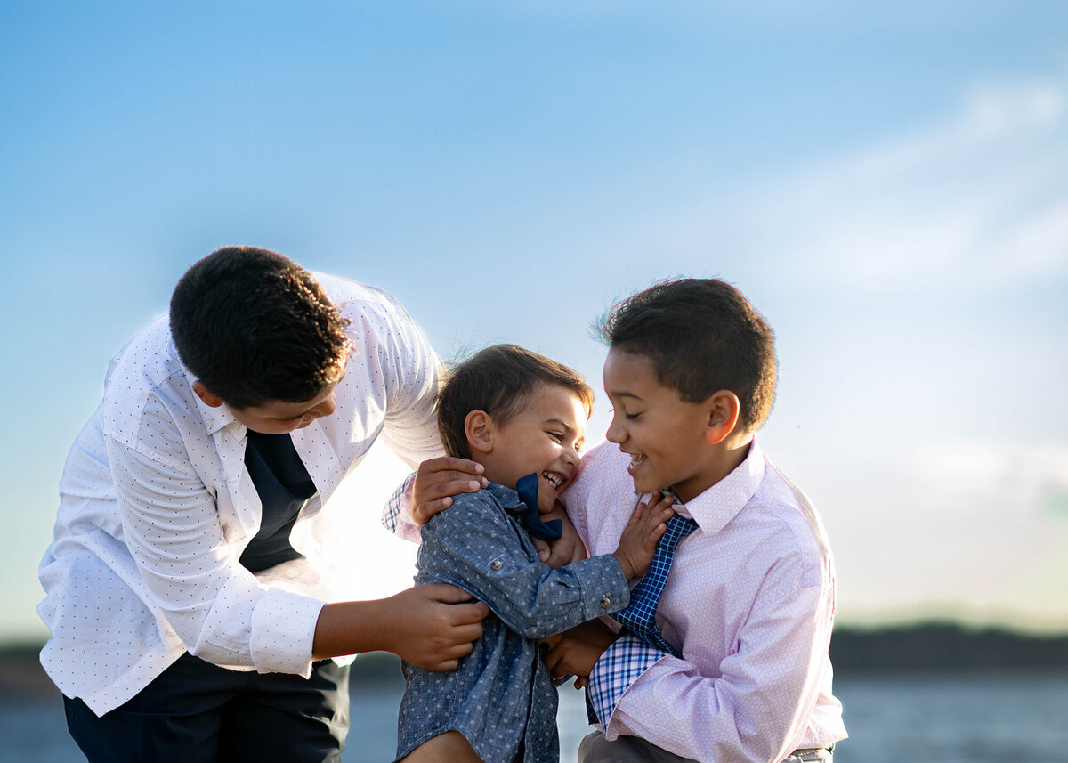 3 brothers tickle each other and laugh next to a lake