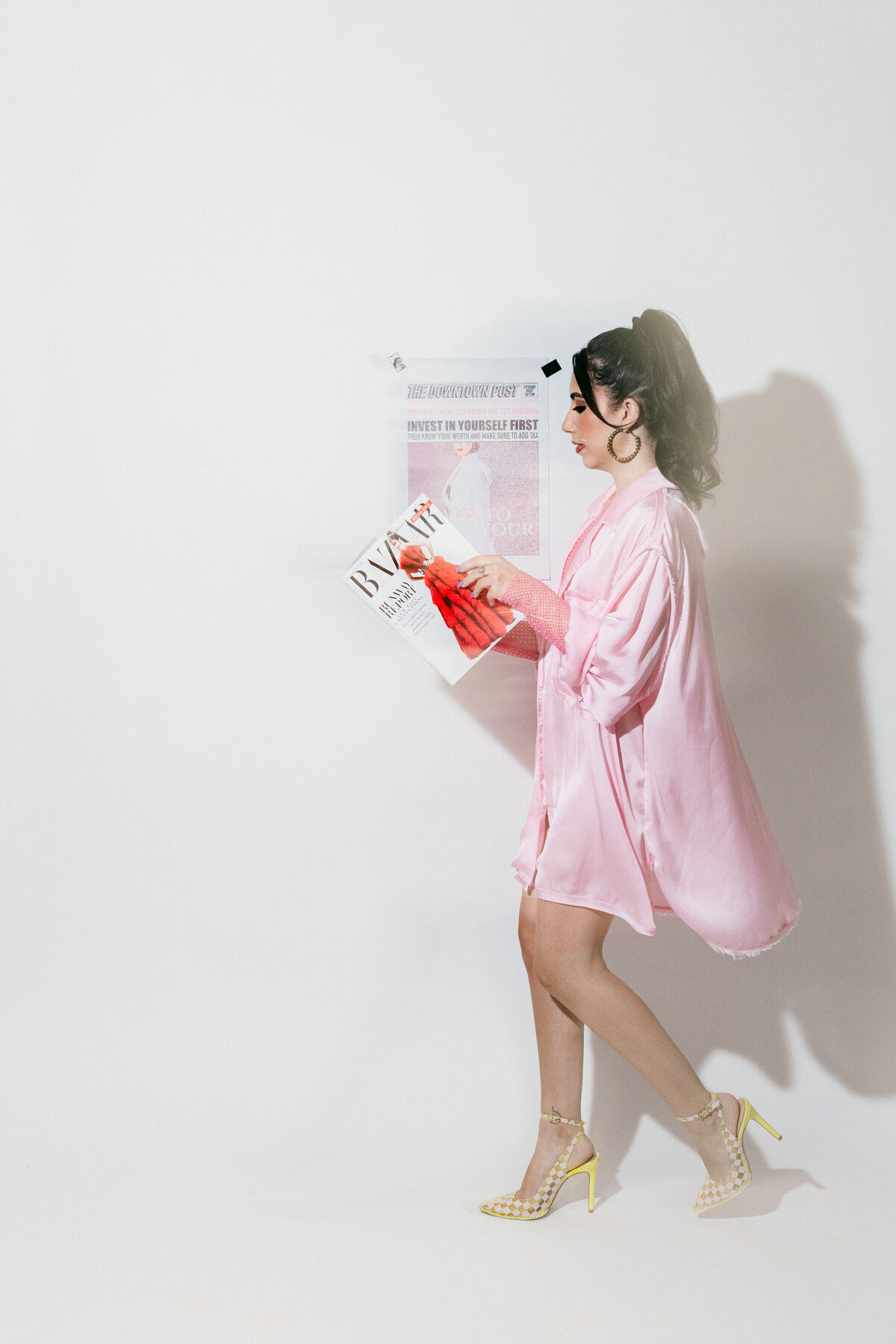 Editorial-style branding photo of a woman in a pink robe and yellow heels reading BYRDIE magazine against a white backdrop — bold, modern, and beauty-industry focused.