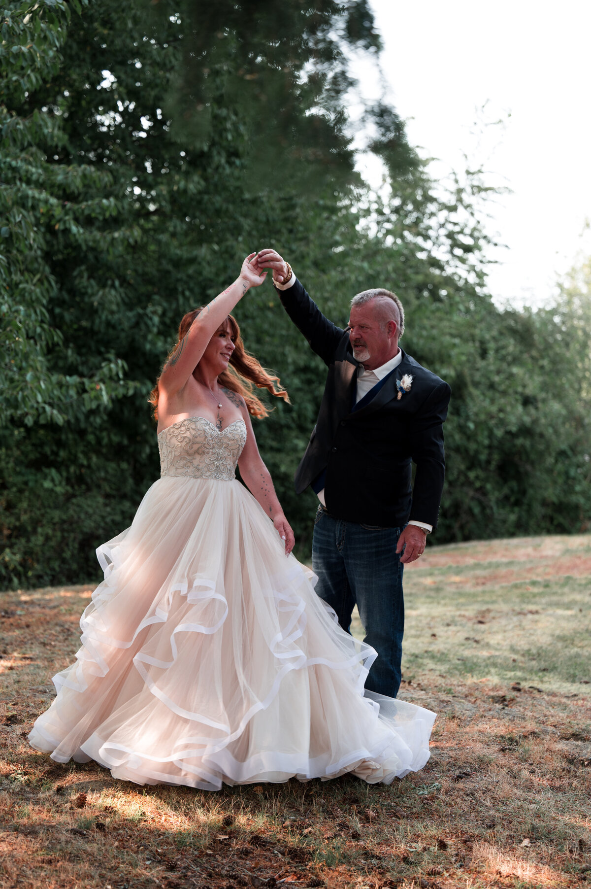 Bride and groom dance in a field surrounded by lush green trees on Vancouver Island