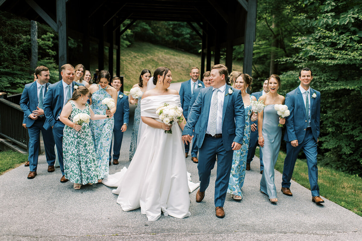 Wedding party walking across the covered bridge, bridesmaids in blue and floral dresses and groomsmen in blue suits.
