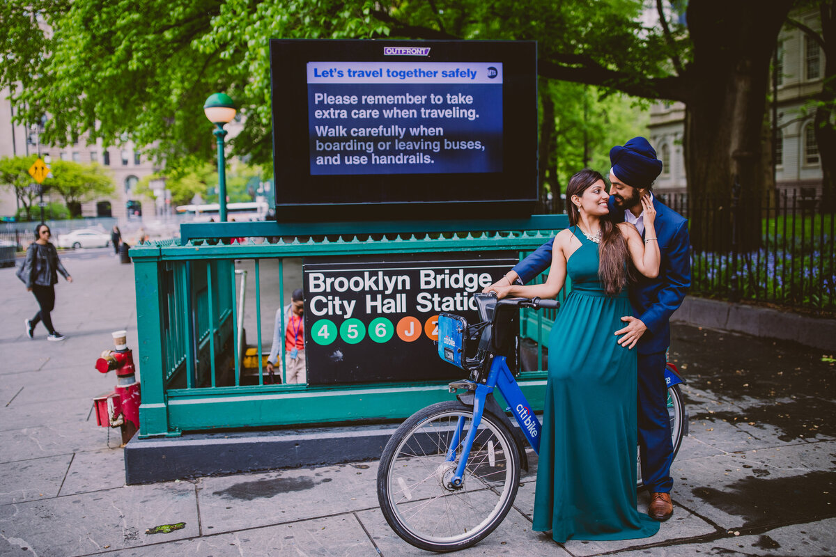 A sikh engagement couple sitting on a citibike in front of the subway station in brooklyn city hall