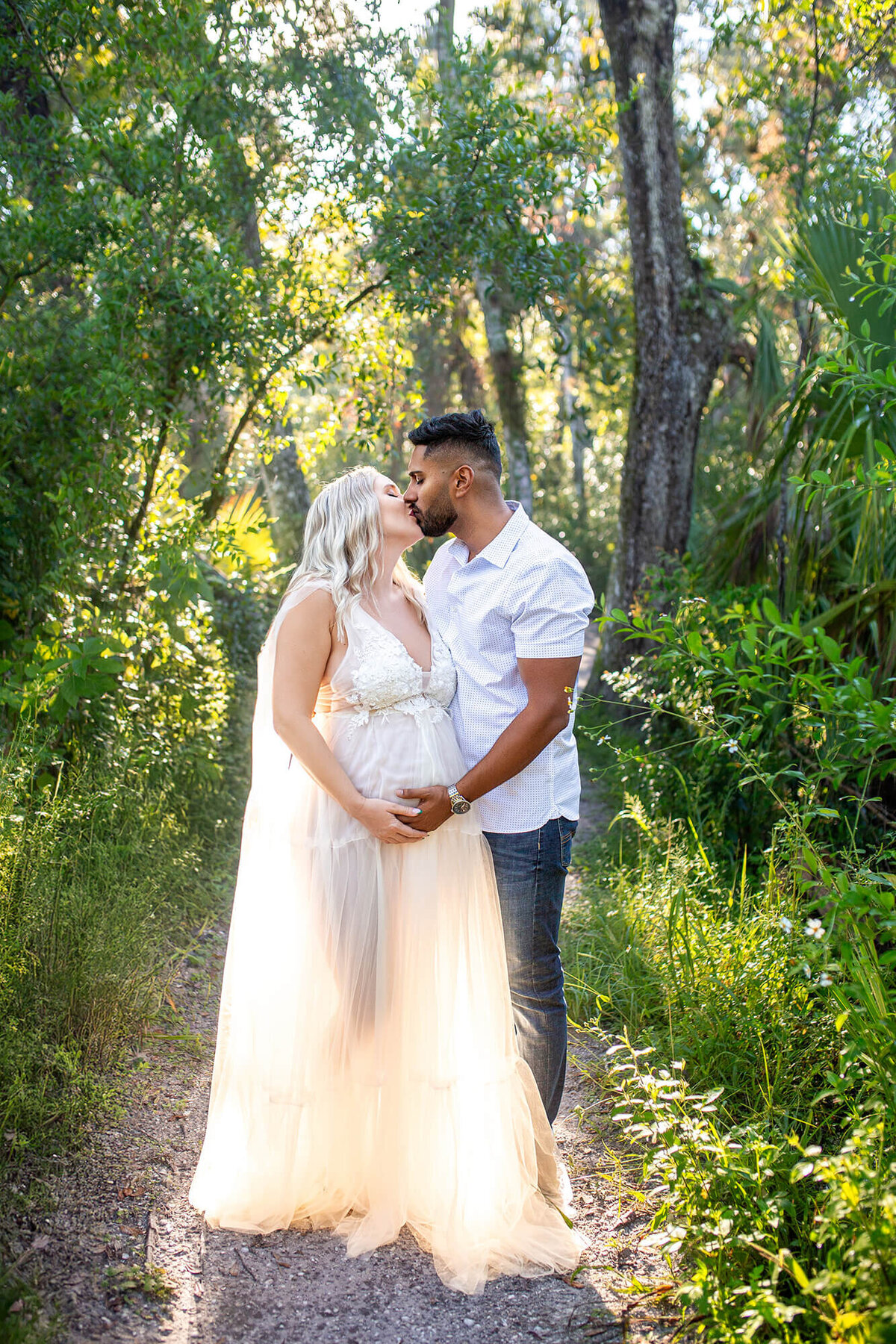 Blond pregnant woman and dark haired man holding belly while kissing in golden light. Captured by Tampa maternity photographer Sarah Wyndham Photography