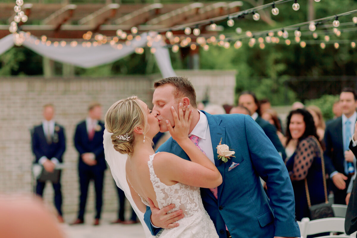 A newlywed couple kissing as they stand in the middle of the aisle after their wedding ceremony 