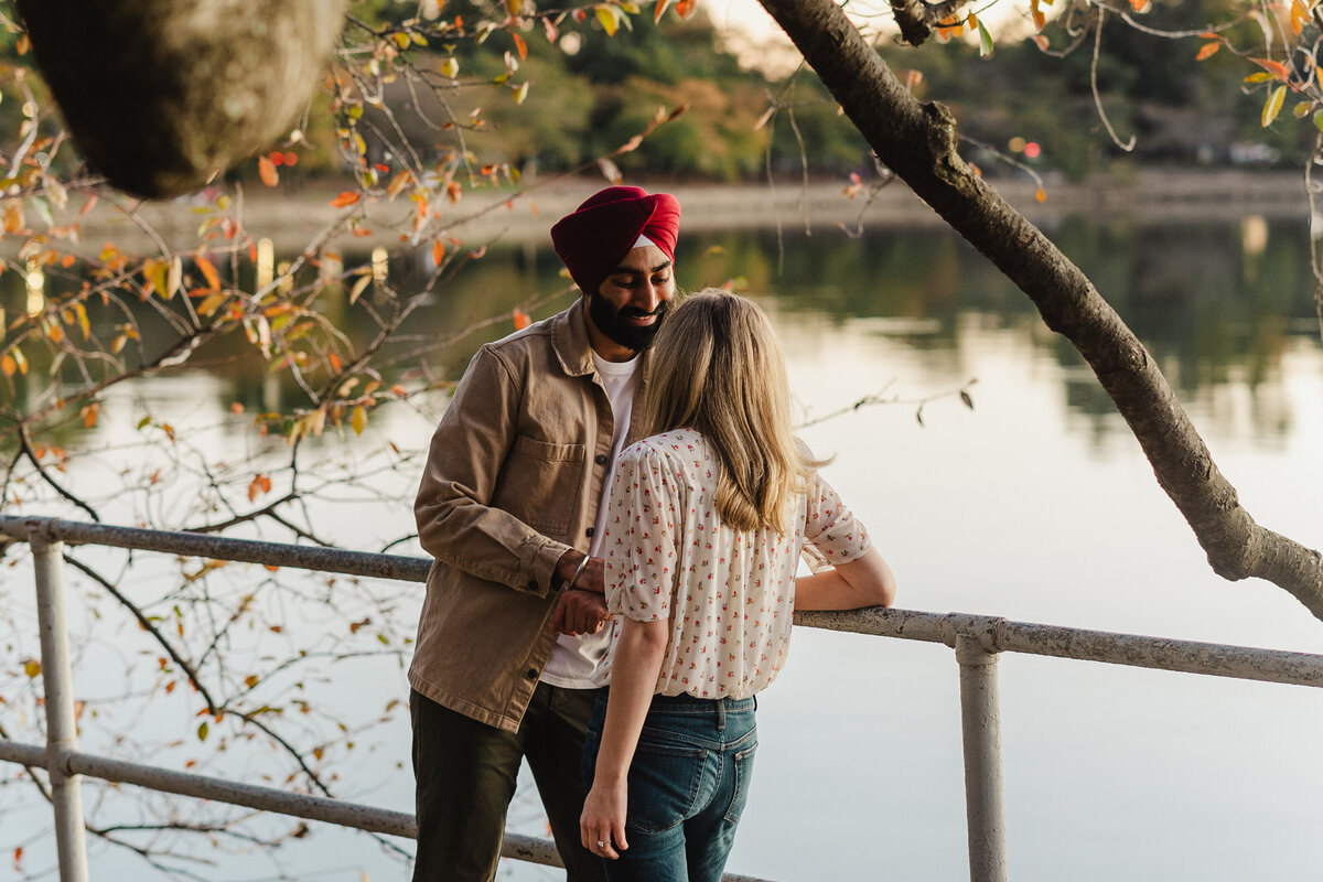 An engaged couple leans against a pole.
