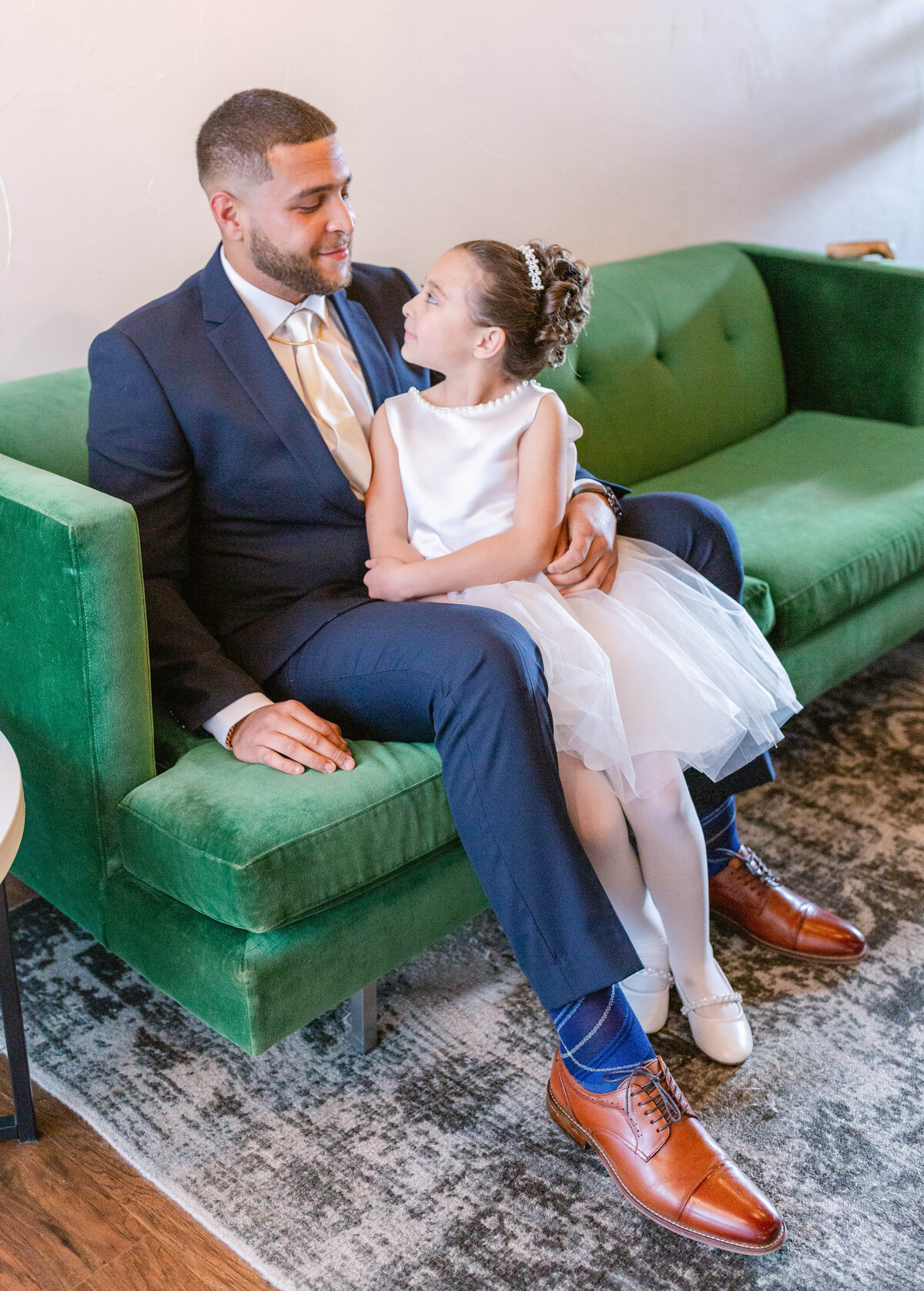 Groom and daughter sitting on couch during getting ready photos at The Refinery at 120 in Culpeper, Virginia.
