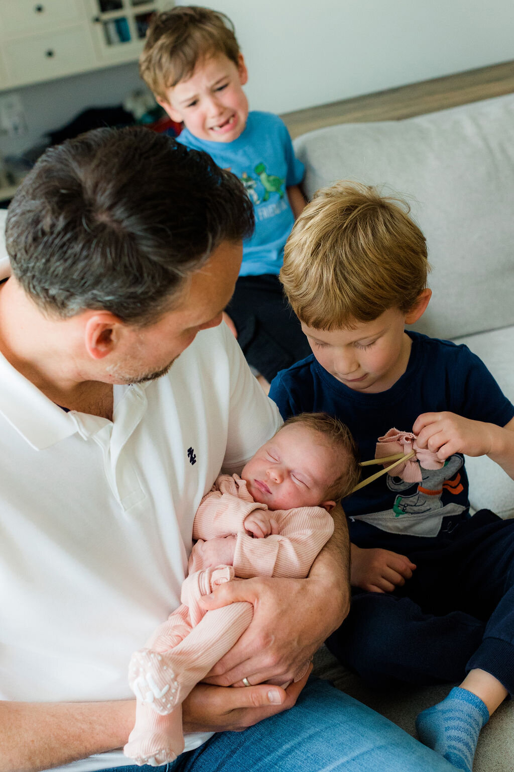 A father holds his newborn child while their younger brothers look on.