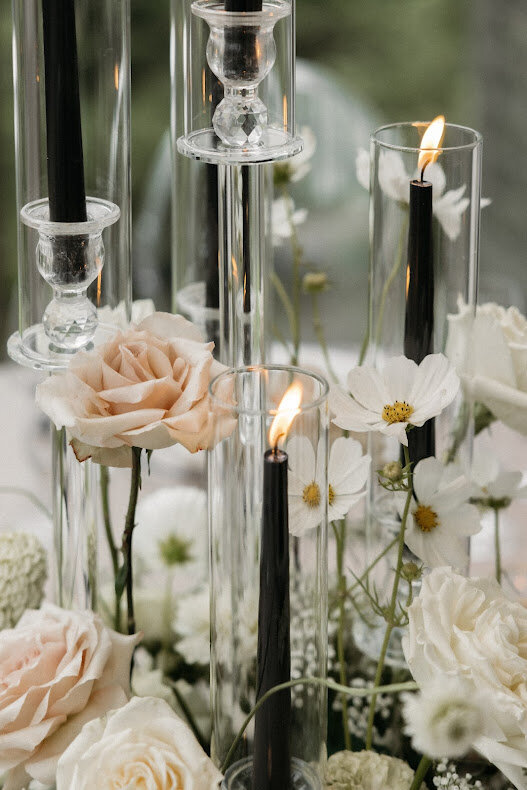 Close-up of a wedding centerpiece featuring three lit black tapered candles and beautiful taupe and white flowers at the National Arts Centre’s O'Born Room.