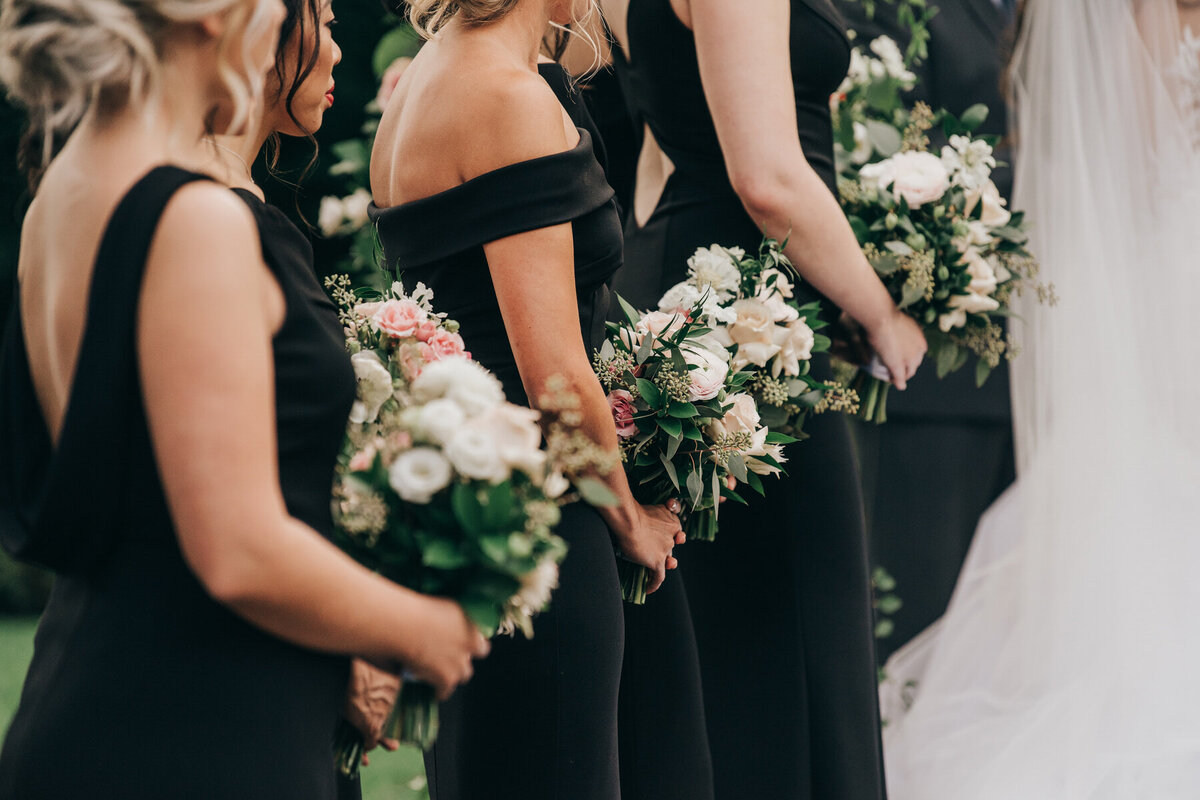 Bridesmaids in black dresses holding luxurious pink and white bouquets