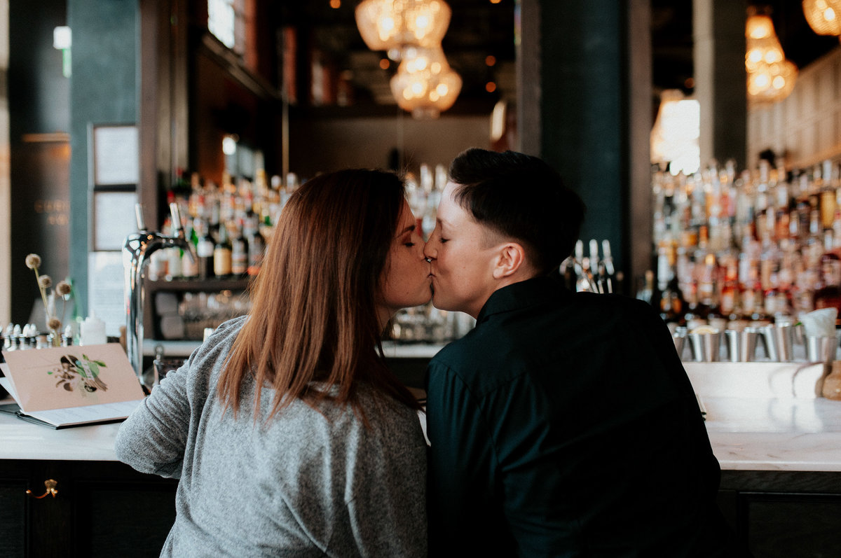 Same sex couple kissing in bar for engagement photo shoot