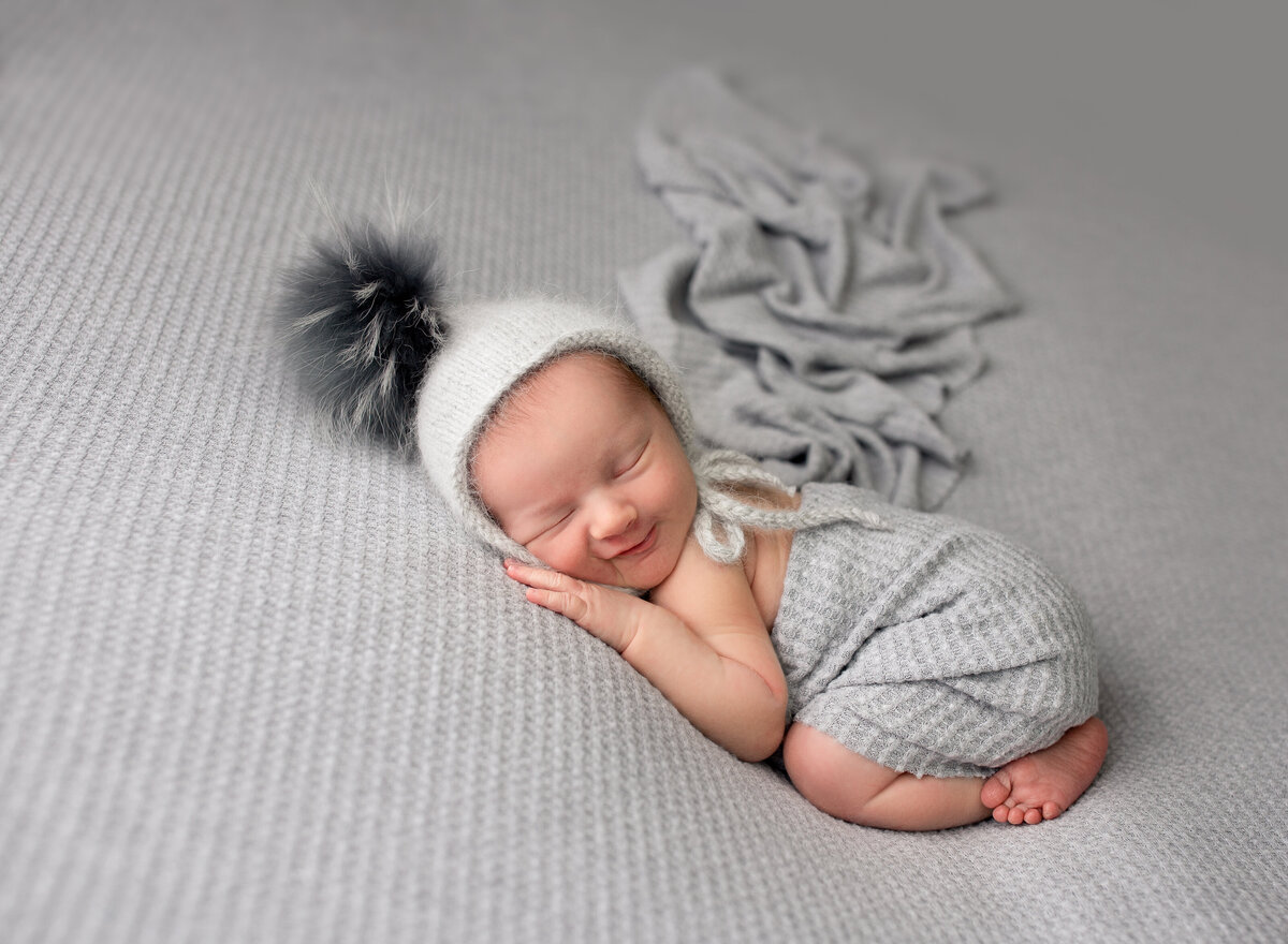 A sleeping baby smiles on a grey backdrop.