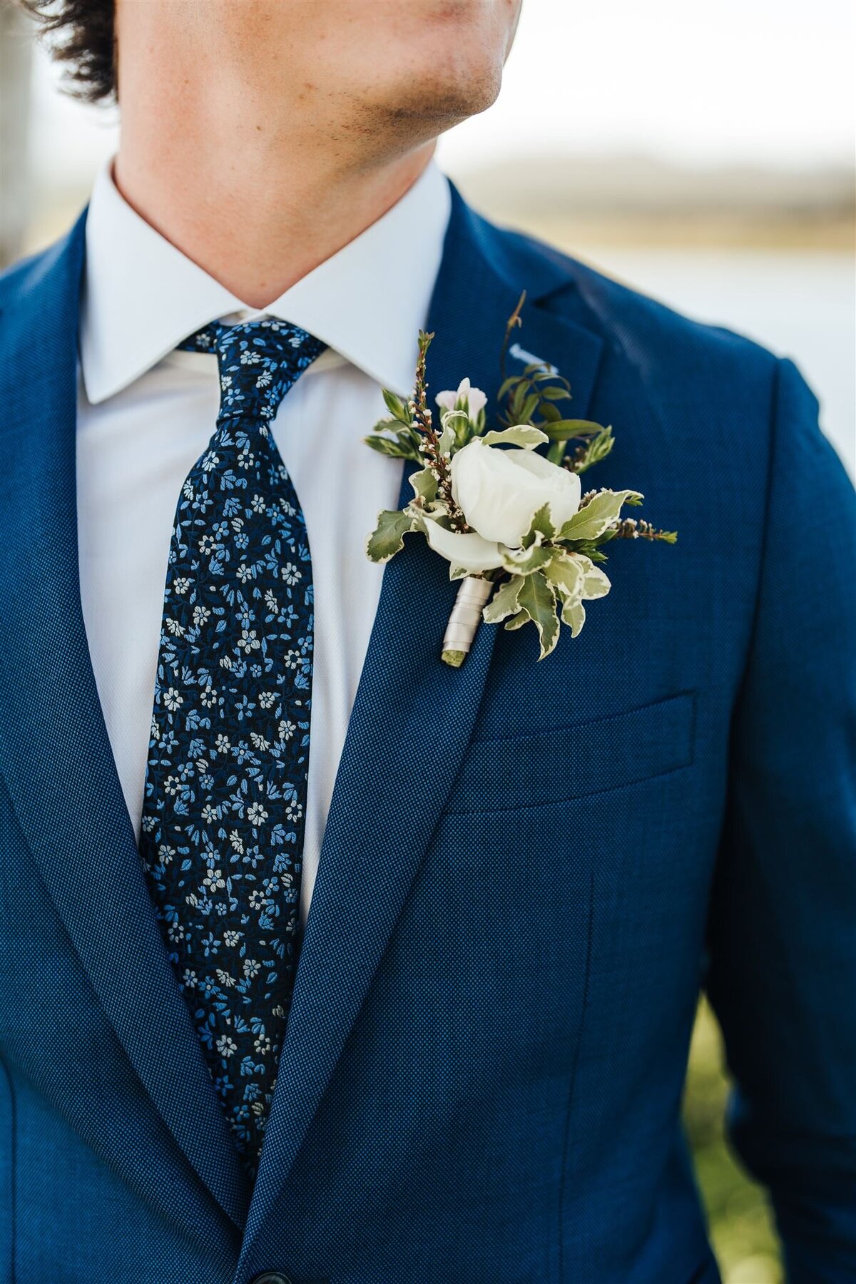 White ranunculus boutonniere with mixed greenery  with blue floral tie