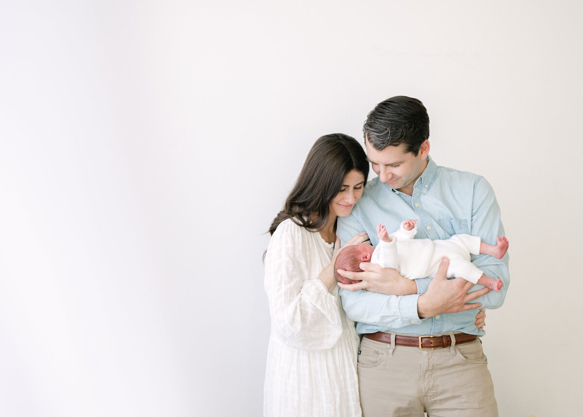 Family laying down and snuggling in a field holding their baby up in the air and smiliing at her- photo by Maegan R Photography