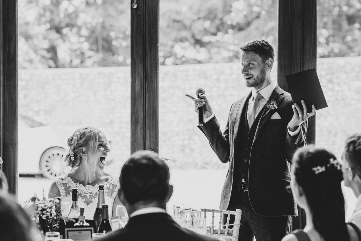 Groom giving his speech, whilst bride laughs