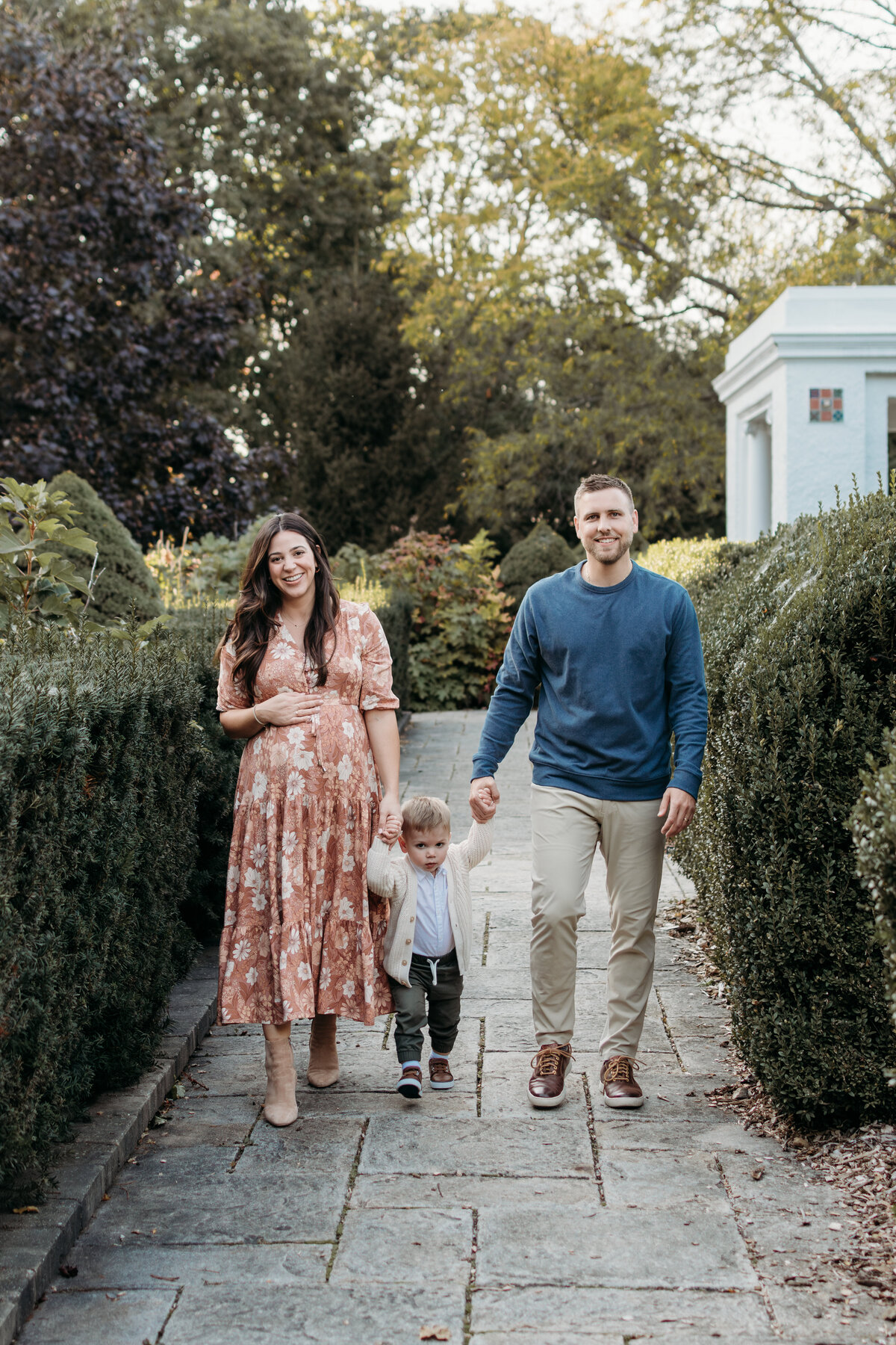 Family walking amongst some beautiful greenery with their toddler boy and baby girl in the belly during a maternity photoshoot in WHeaton, IL
