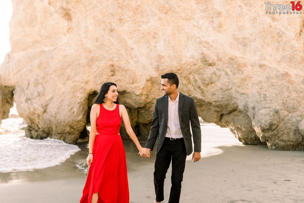 Newly engaged couple walk along the beach holding hands