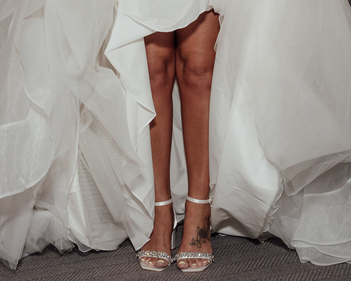 A brides legs and shoes with her dress bunched up behind.