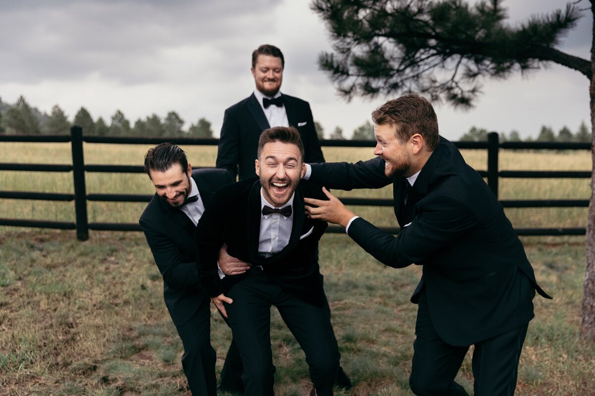 Groom and groomsmen in black suits pose together for photos on his wedding day.