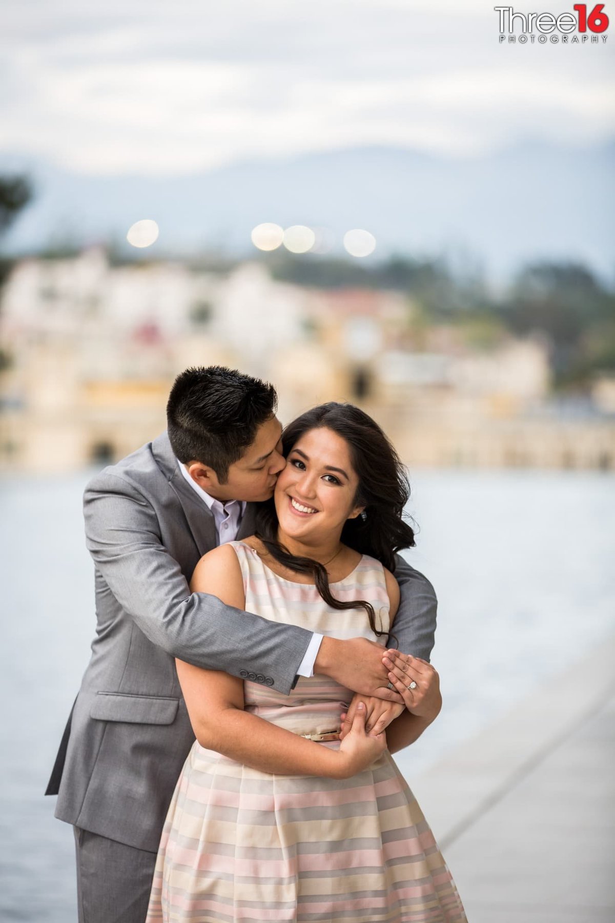 Groom to be kisses his fiance on her cheek during photo shoot