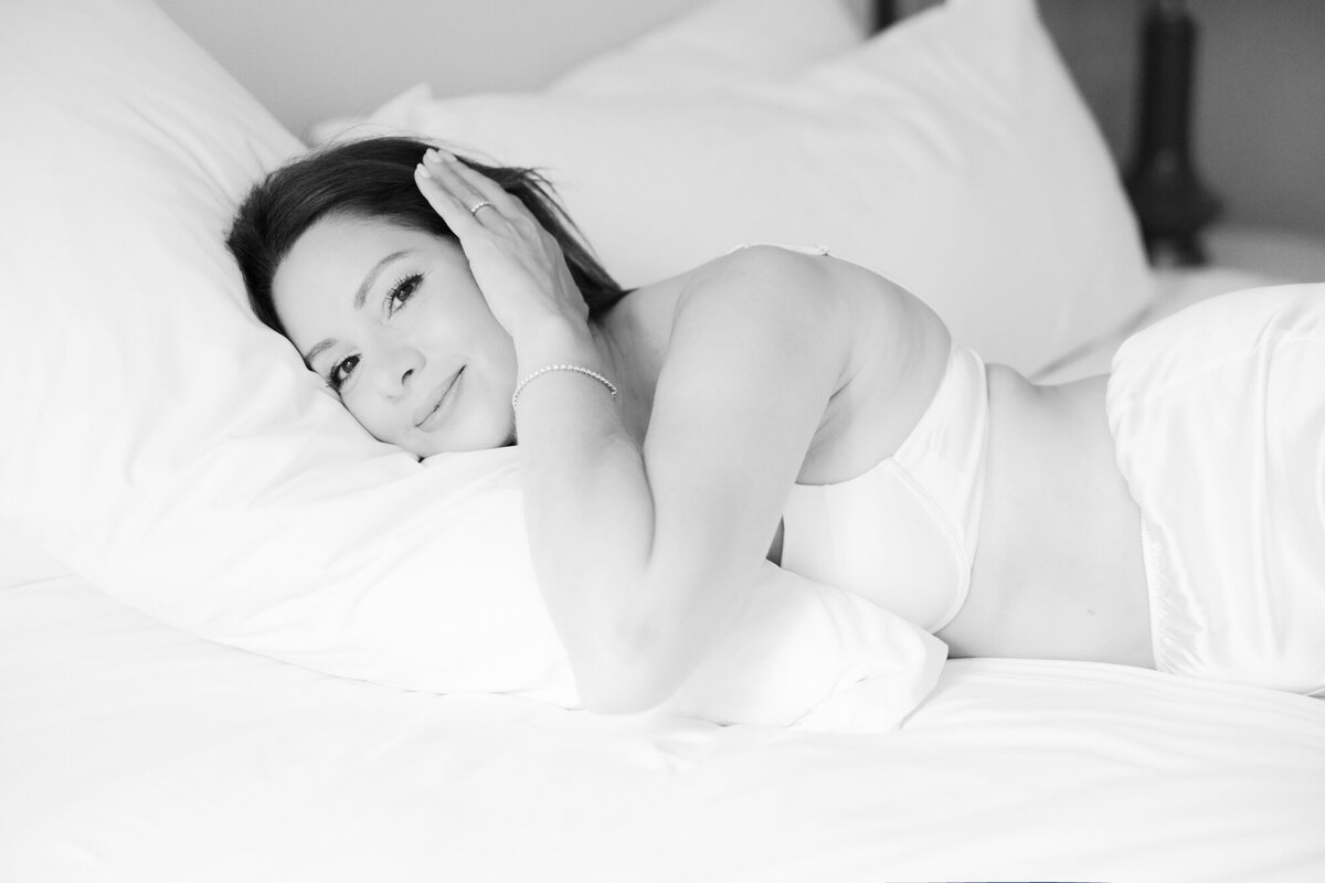 Relaxed boudoir photo of woman in white satin pajamas on bed at the Talbott Hotel