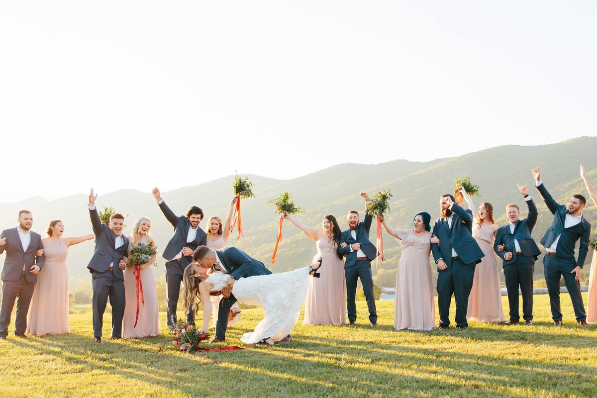 Bridal party cheer as bride and groom dip kiss during golden hour at crooked river wedding