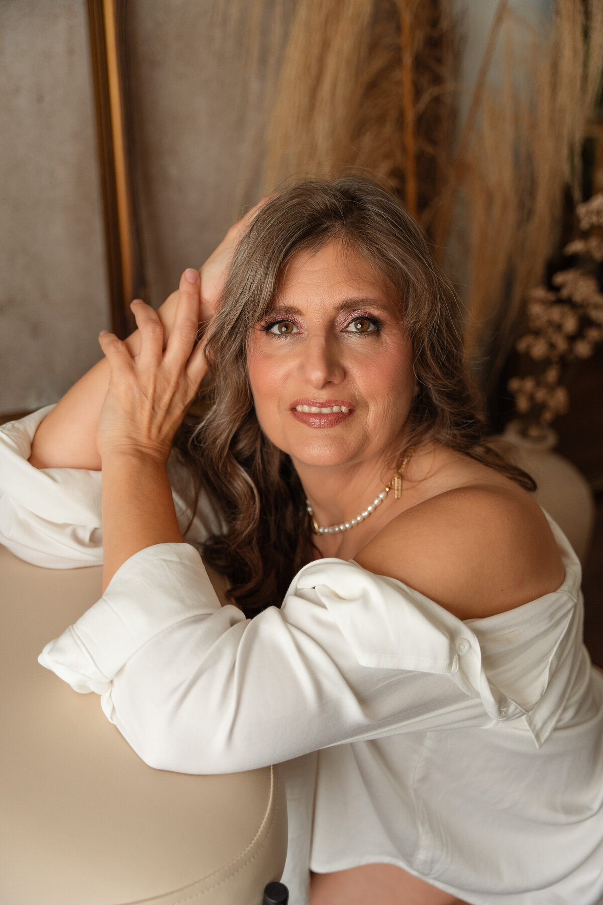 woman with grey hair wearing a white shirt off the shoulders, hands by her face