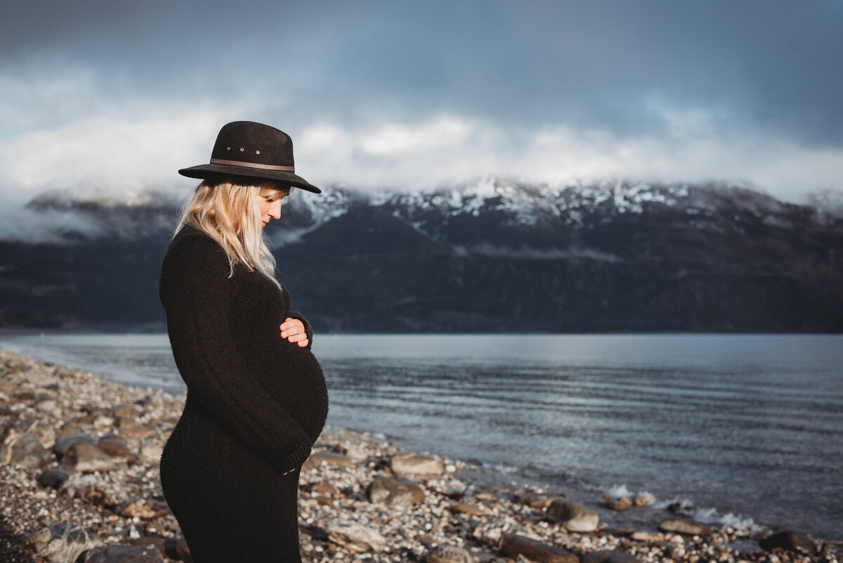 Maternity photoshoot at Lake Wanaka. Pregnant woman standing on the shore of the lake.