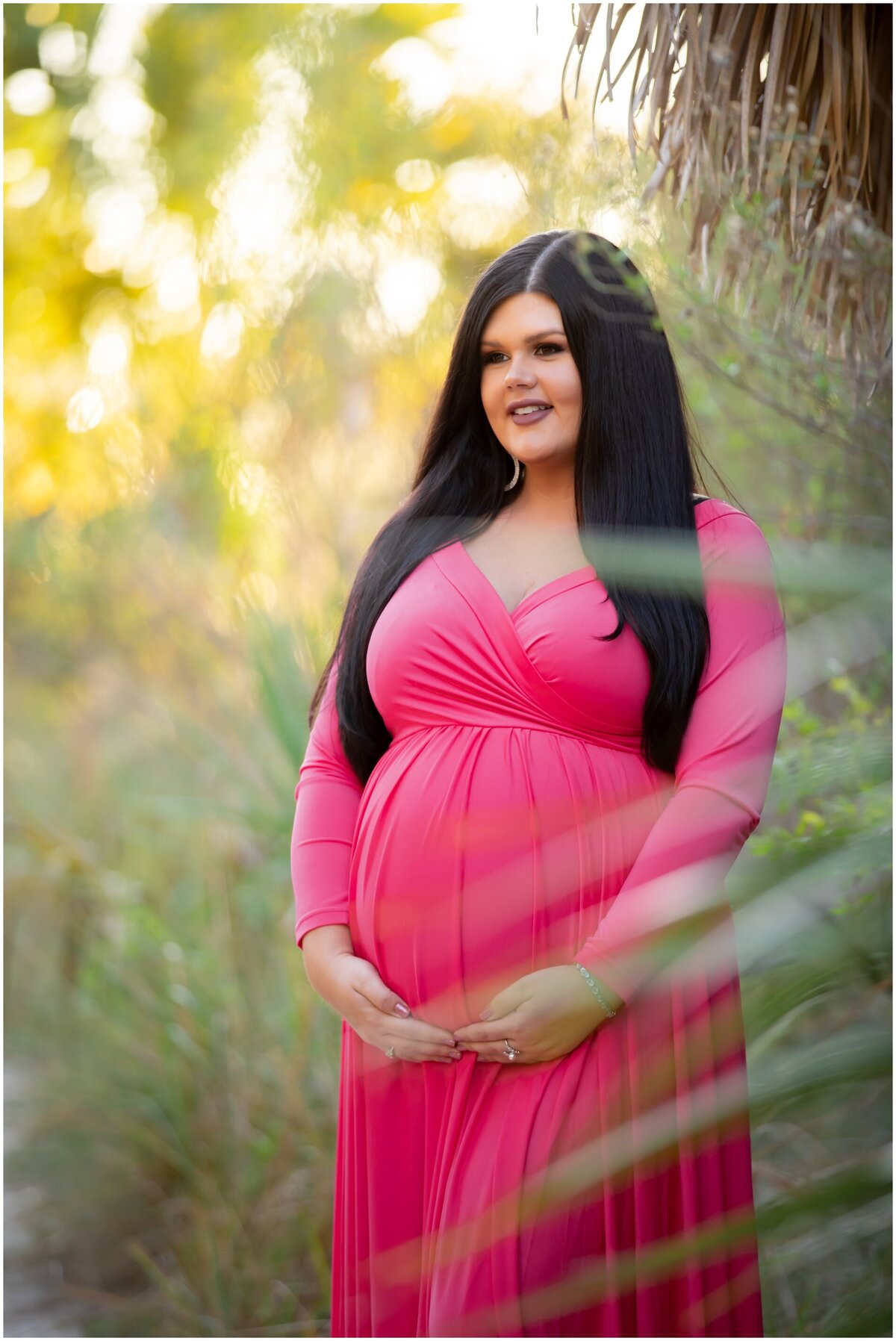 pregnant women in bright pink dress with palm frond in the foreground
