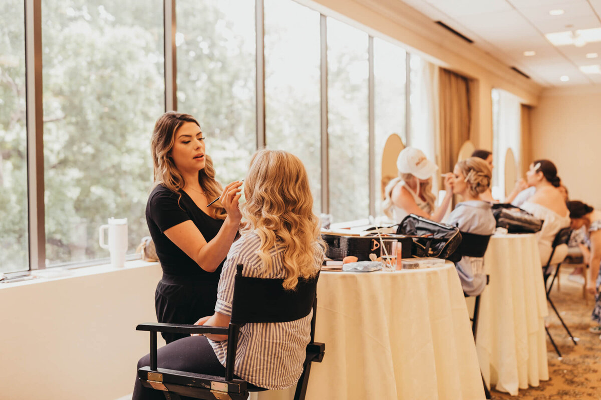 bridesmaids facing the window of trees, getting their hair and makeup done.