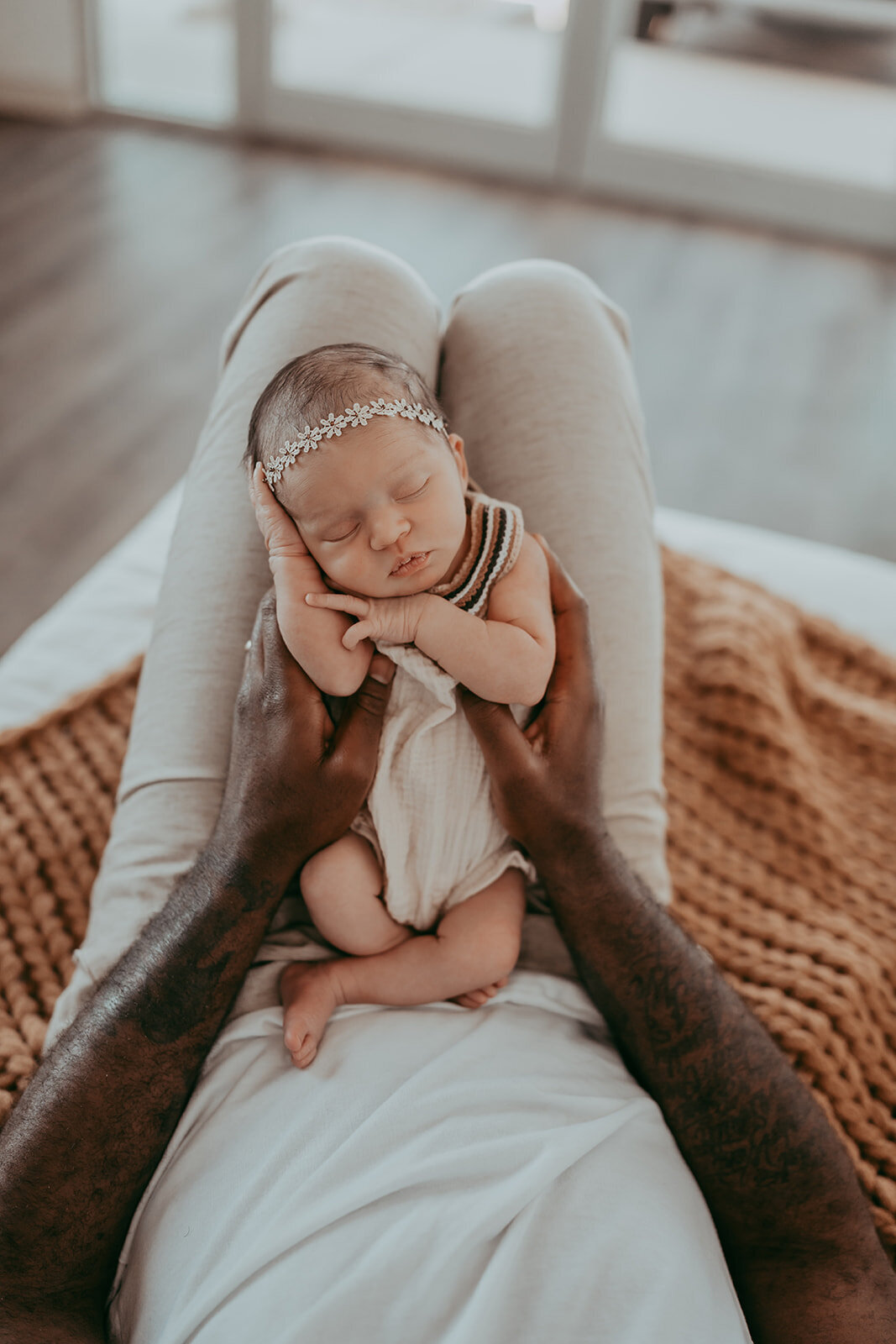 father holds up adorable newborn baby as she sleeps on his knees
