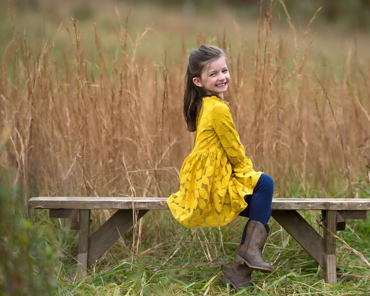 young girl smiling on bench in field