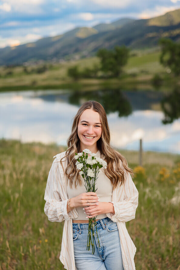 Girl holds flowers in front of her with a lake and mountains behind her in Colorado.
