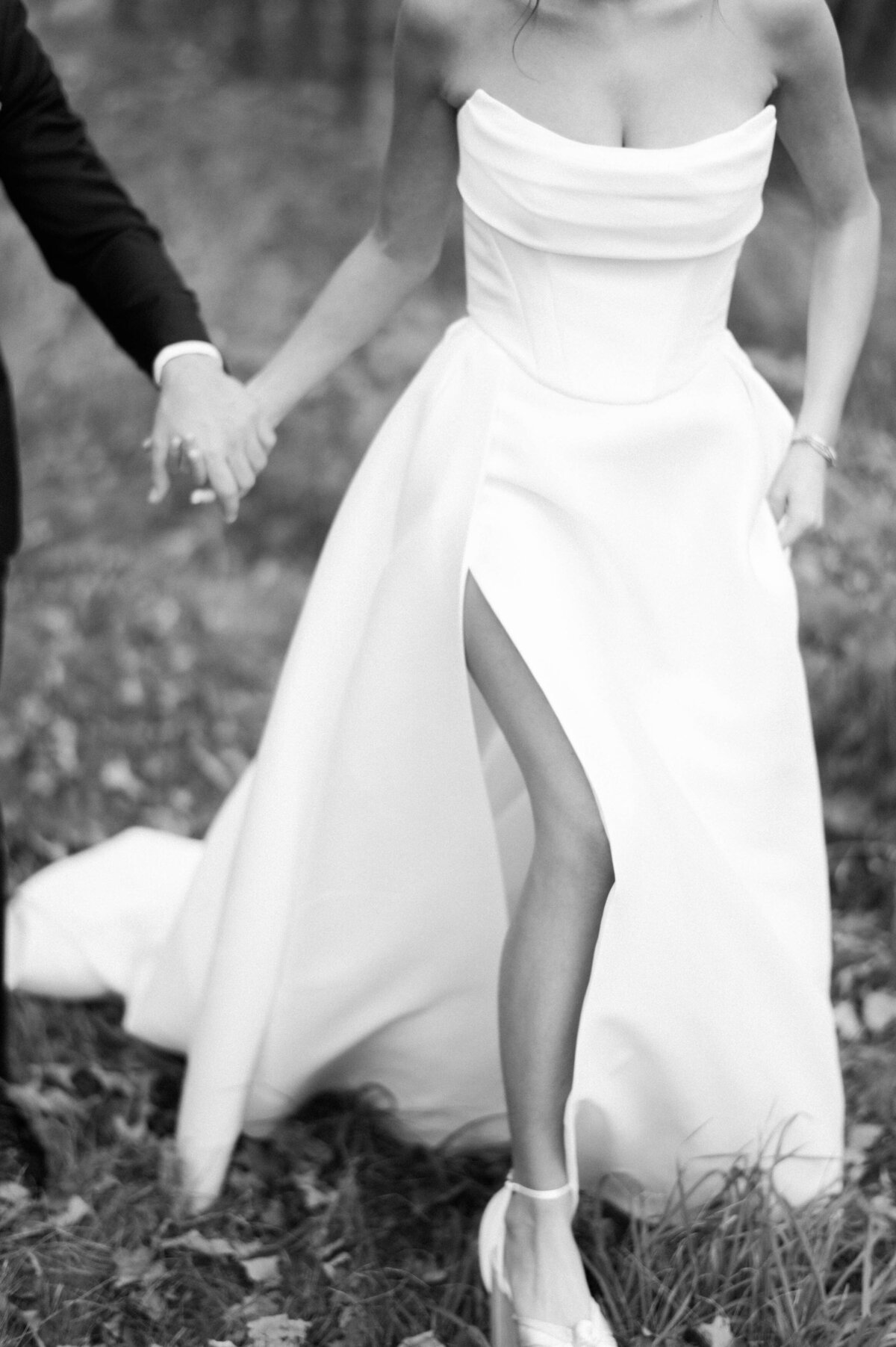 the bride walking hand-in-hand with the groom, revealing a thigh-high slit in her elegant strapless wedding gown